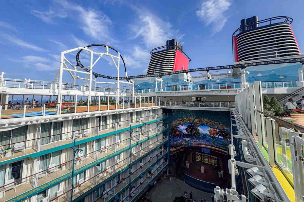 A wide view from the upper deck shows stateroom balconies overlooking a central courtyard stage area with walkways and seating. This perspective helps visualize Disney Adventure cruise layout and verandah room views.