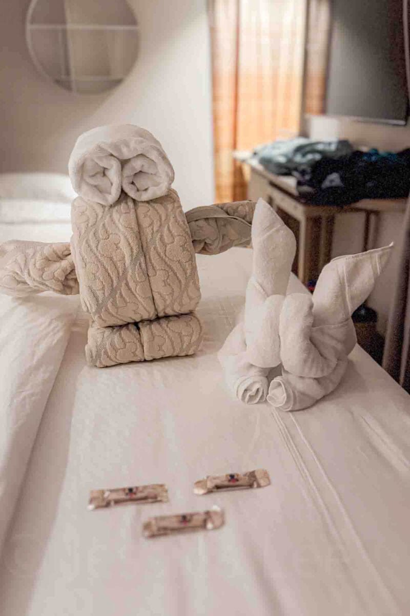 Towels folded into a character resembling Wall-E sit on a bed alongside another folded towel animal. This detail highlights creative housekeeping touches on a Disney cruise.