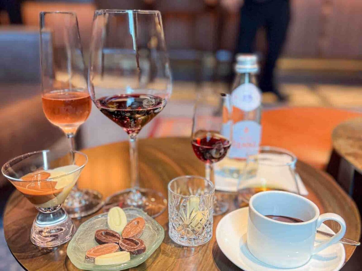 A tasting setup includes glasses of wine, liqueur, chocolate pieces, and melted chocolate arranged on a wooden tray. This experience showcases an adults only chocolate and liquor tasting on a Disney cruise.