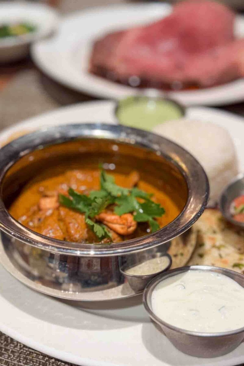 A silver bowl of chicken korma garnished with cilantro is served with rice, naan, and dipping sauces on the side. This meal showcases flavorful Indian cuisine available on a Disney cruise.