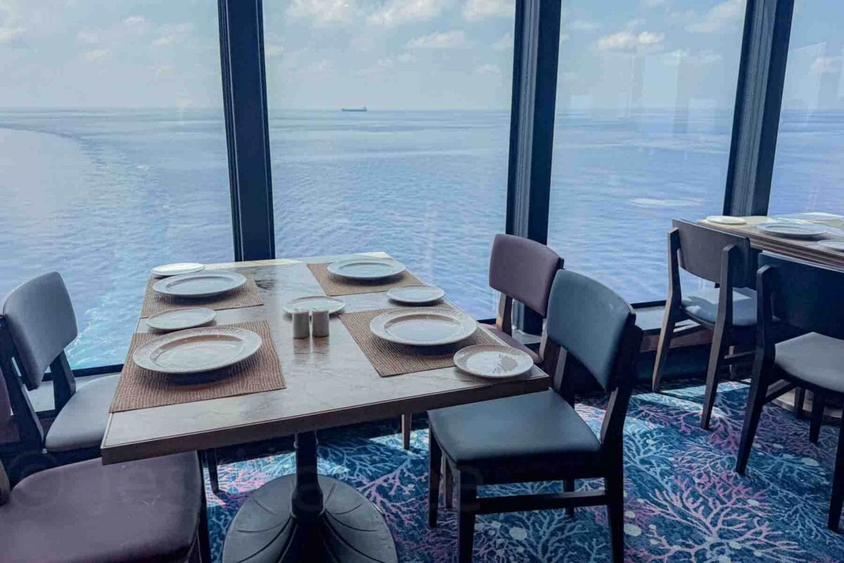 A dining table set with plates sits beside large windows overlooking the open ocean. This seating area highlights scenic dining views available on a Disney cruise.