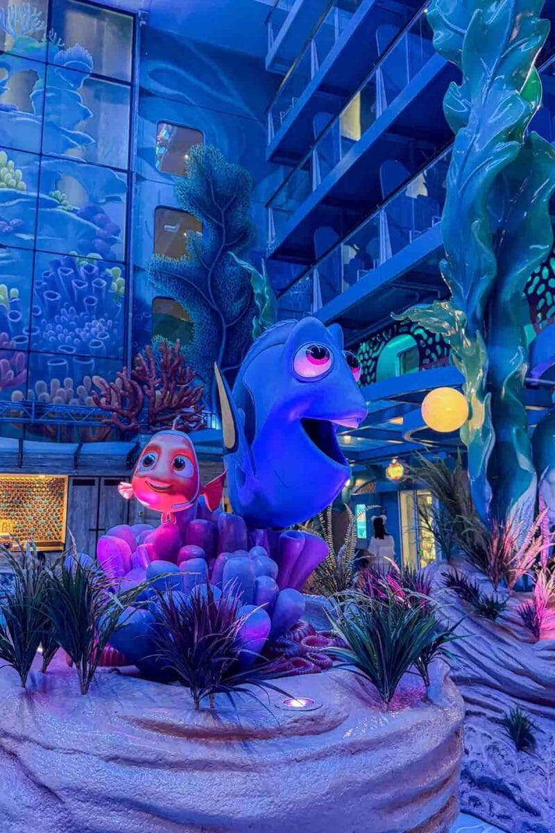 A colorful display of Dory and Nemo characters is surrounded by coral and underwater themed decor in a bright atrium, Discovery Reef. This area highlights immersive themed spaces on the Disney Adventure cruise.