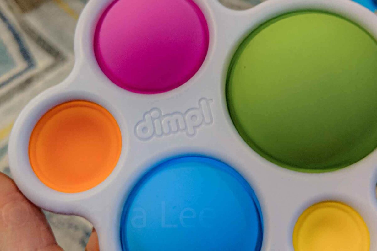 Close up of an original Fat Brain Toys “dimpl” silicone pop toy with colorful buttons, a quiet and engaging choice among best airplane toys for babies.