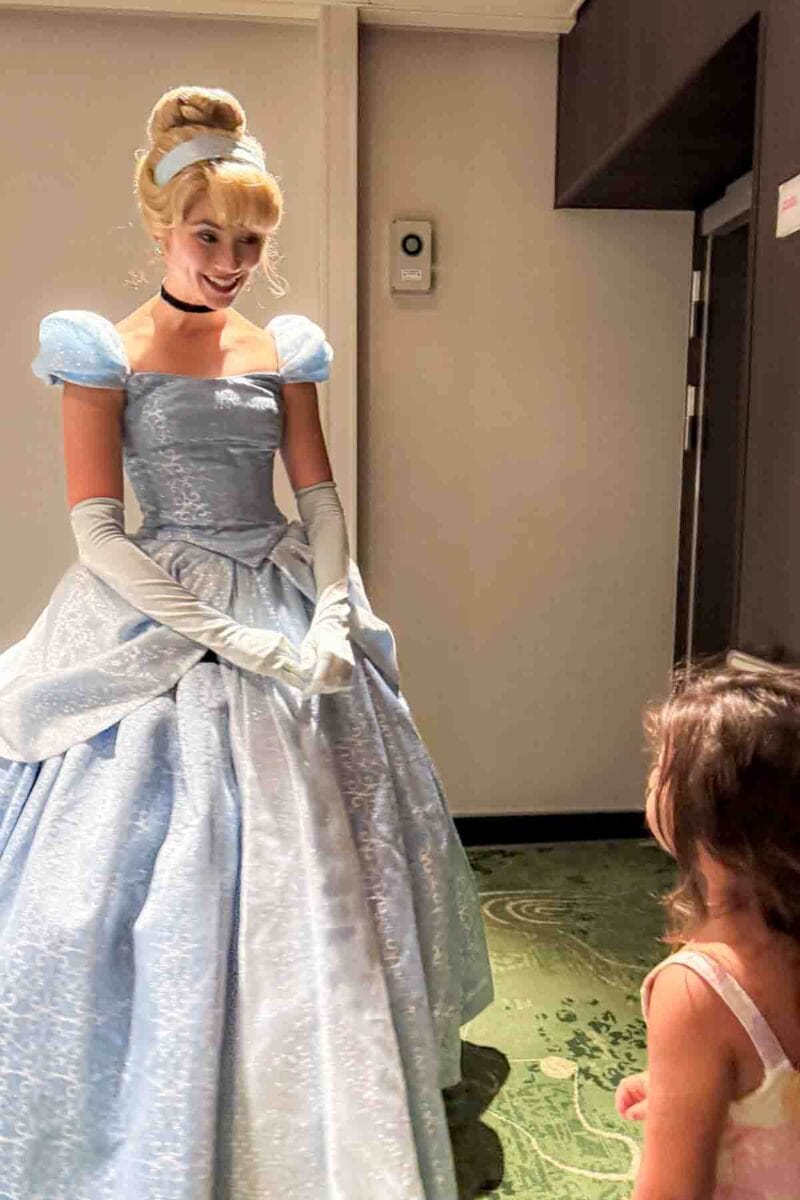 Cinderella in a classic blue ball gown smiles and speaks to a young child during a character meet and greet. This interaction highlights princess experiences on a Disney cruise.