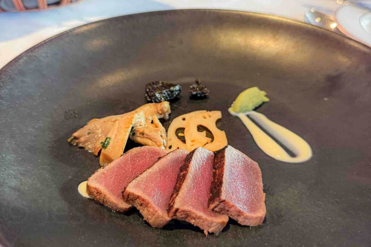 A plated appetizer features slices of seared tuna alongside vegetables and a light sauce on a dark gray dish. This presentation highlights upscale dining available on a Disney cruise.