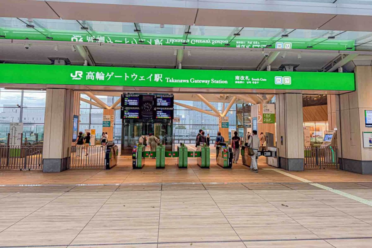 Entrance gates at a bright modern station with a large green sign reading "Takanawa Gateway Station" above ticket gate barriers. Stations like this highlight how easy it is getting around Tokyo with kids using their organized train system.