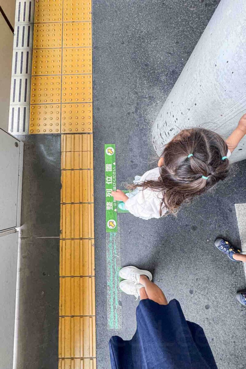 Overhead shot of a toddler standing beside an adult at a waiting line on a. train platform in Tokyo.
