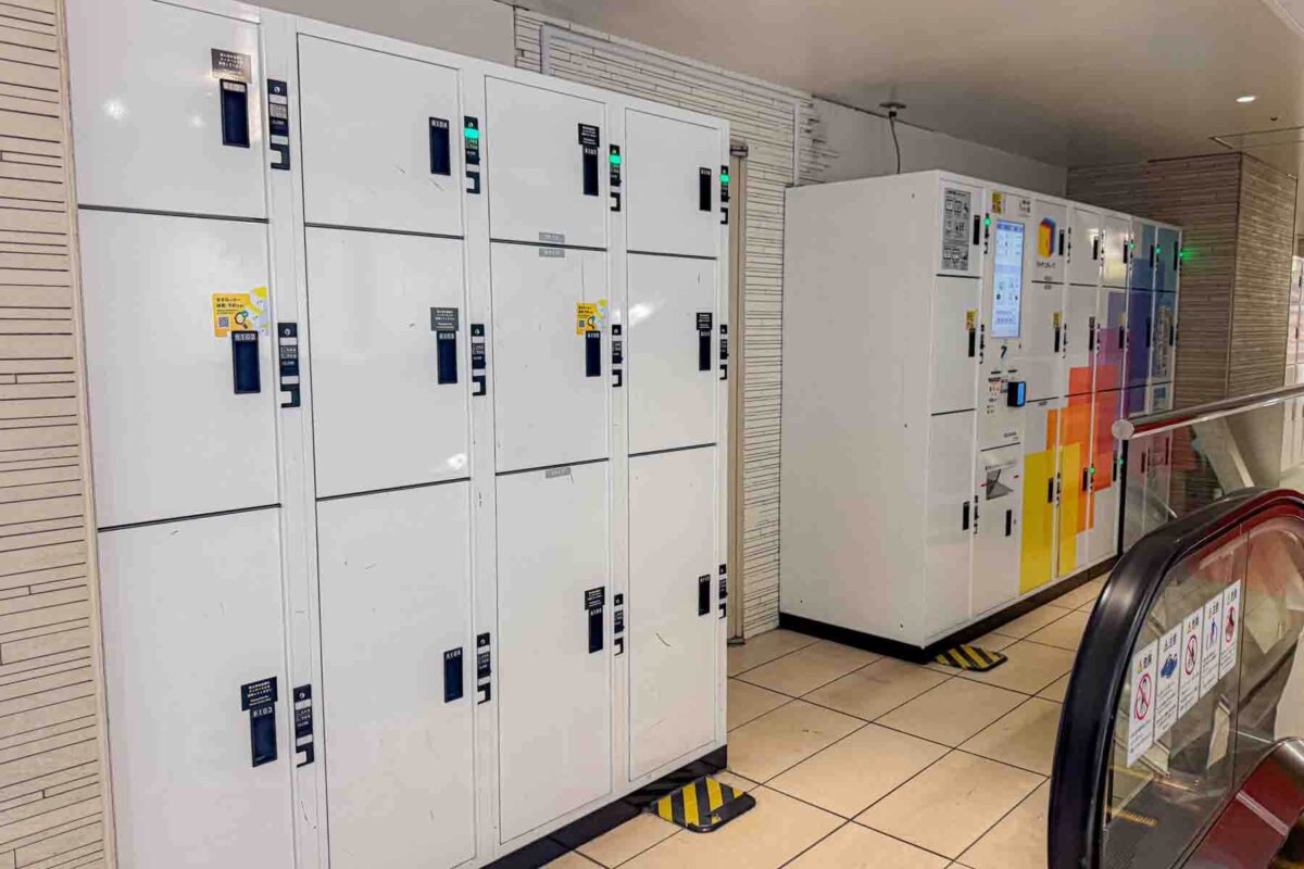 Rows of white coin lockers and a ticket machine inside Tokyo Station near an escalator provide convenient storage for travelers. These lockers are useful when wanting to hang out and explore Tokyo Station when transiting through with luggage.