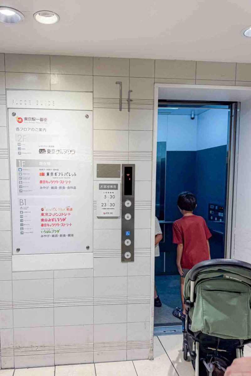 Children walk into a small elevator with a travel stroller following them as they navigate down to a train platform. Tokyo train stations can be accessible to strollers.