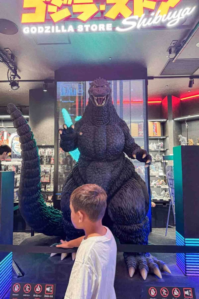 Child standing in front of a large Godzilla statue display inside the Godzilla Store Shibuya at Parco mall in Tokyo. Character themed attractions like this are fun stops for families traveling to Tokyo with kids.
