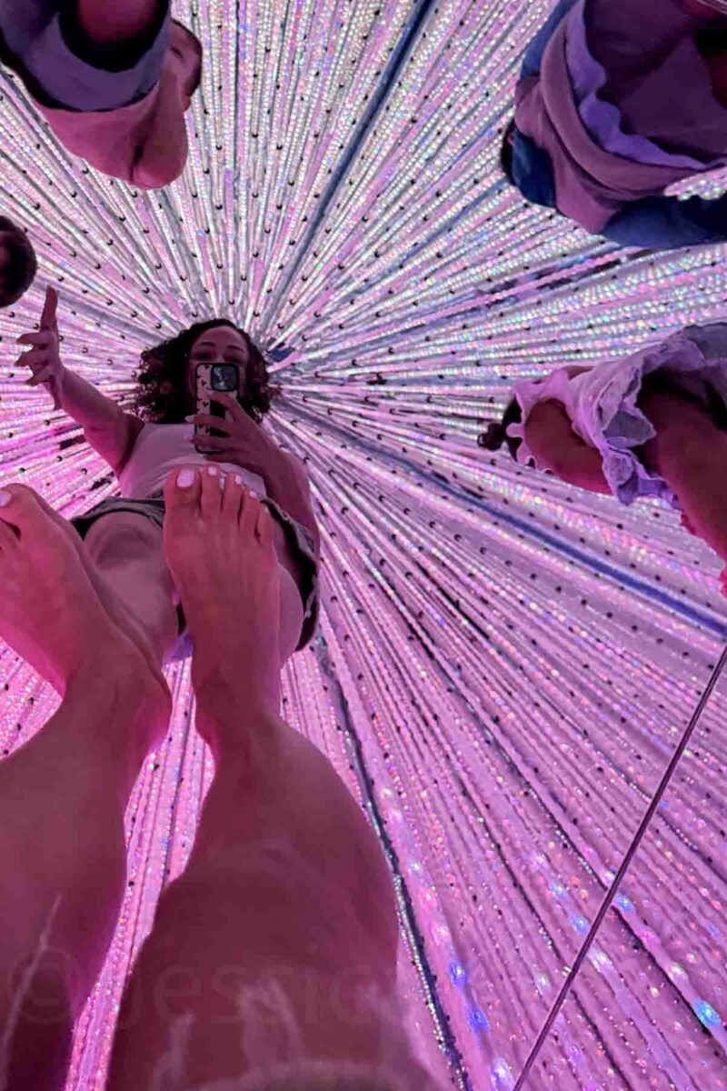 Family reflected inside the mirrored crystal room at teamLab Tokyo with pink hanging lights creating an infinity effect around them. Immersive art experiences like this are popular family activities in Tokyo.
