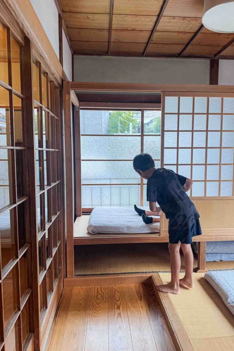 Child sliding a shoji screen inside a traditional Japanese townhouse room with tatami floors, and wooden details. Staying in traditional accommodations can be a memorable part of traveling to Tokyo with kids.