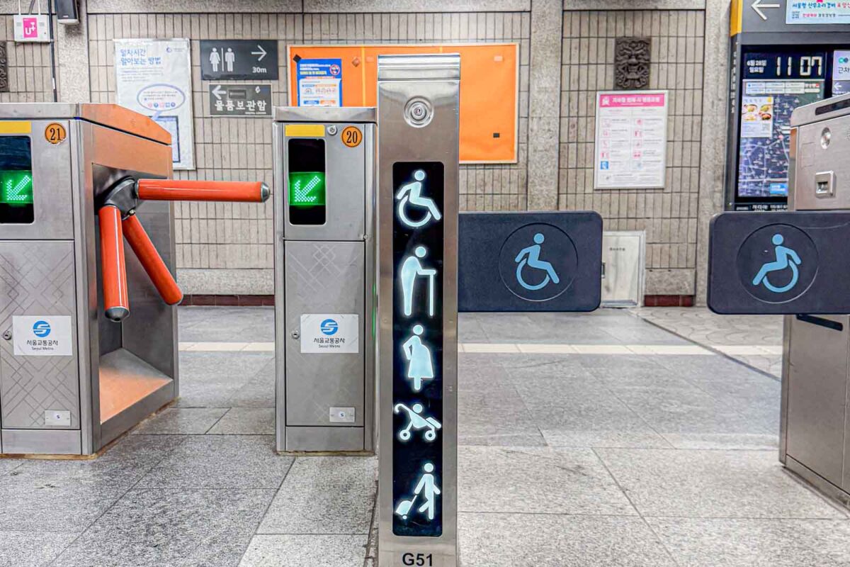 A wide Metro entrance displays illuminated symbols for a wheelchair user. An adult with a child. A stroller. And a person with a cane. The accessible gate gives families more room for strollers and luggage when using the Busan subway with kids.