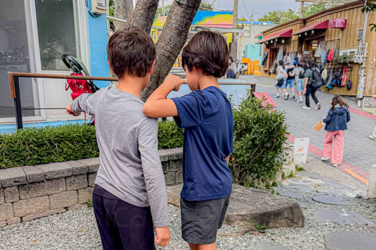 Two children stand on a rough gravel and stone path beside the narrow lanes of Gamcheon Culture Village. The uneven ground is another example of why the final walking portion of a Busan transportation route matters with kids.