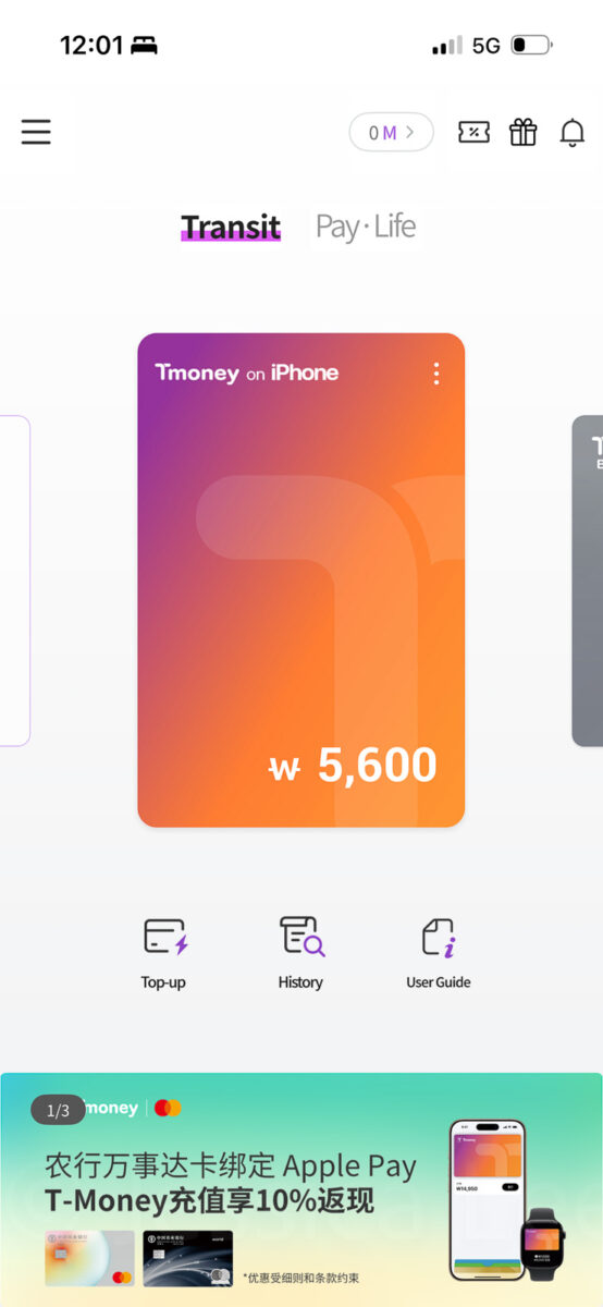 The MobileTmoney app on an iPhone shows a digital transit card with a balance of "₩ 5.600". Other visible labels read "Transit". "Pay Life". "Tmoney on iPhone". "Top up". "History". "User Guide".