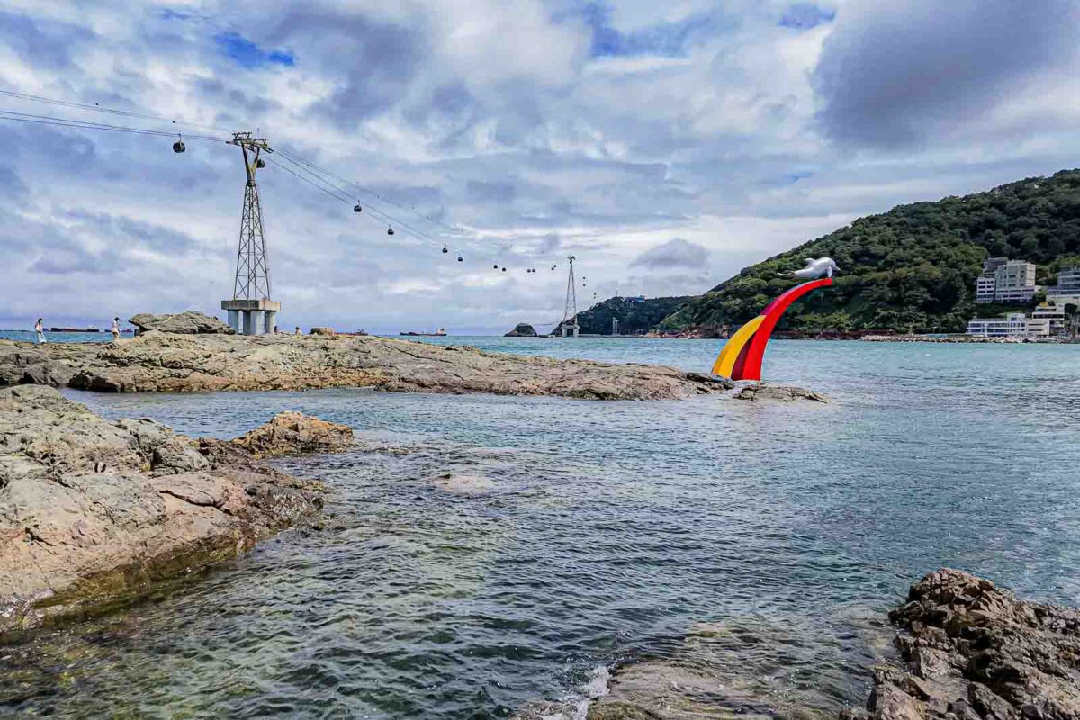 Cable cars travel above the rocky Songdo coastline with a colorful dolphin sculpture rising from the water. Reaching attractions spread across western Busan can make a taxi worthwhile when it avoids a long or awkward public transportation route.