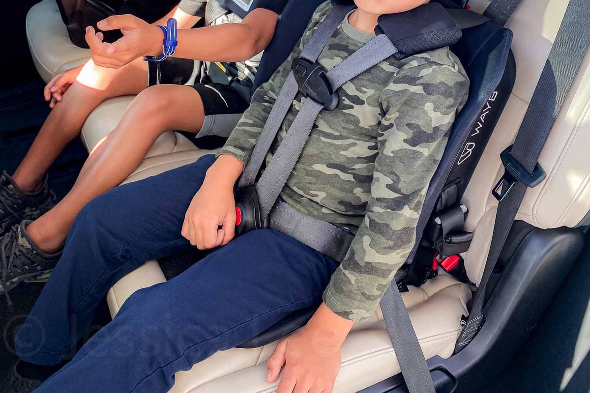 Three children share one vehicle row with a compact Pico car seat beside another child restraint. The narrow setup demonstrates how the seat can work as part of a three-across configuration.