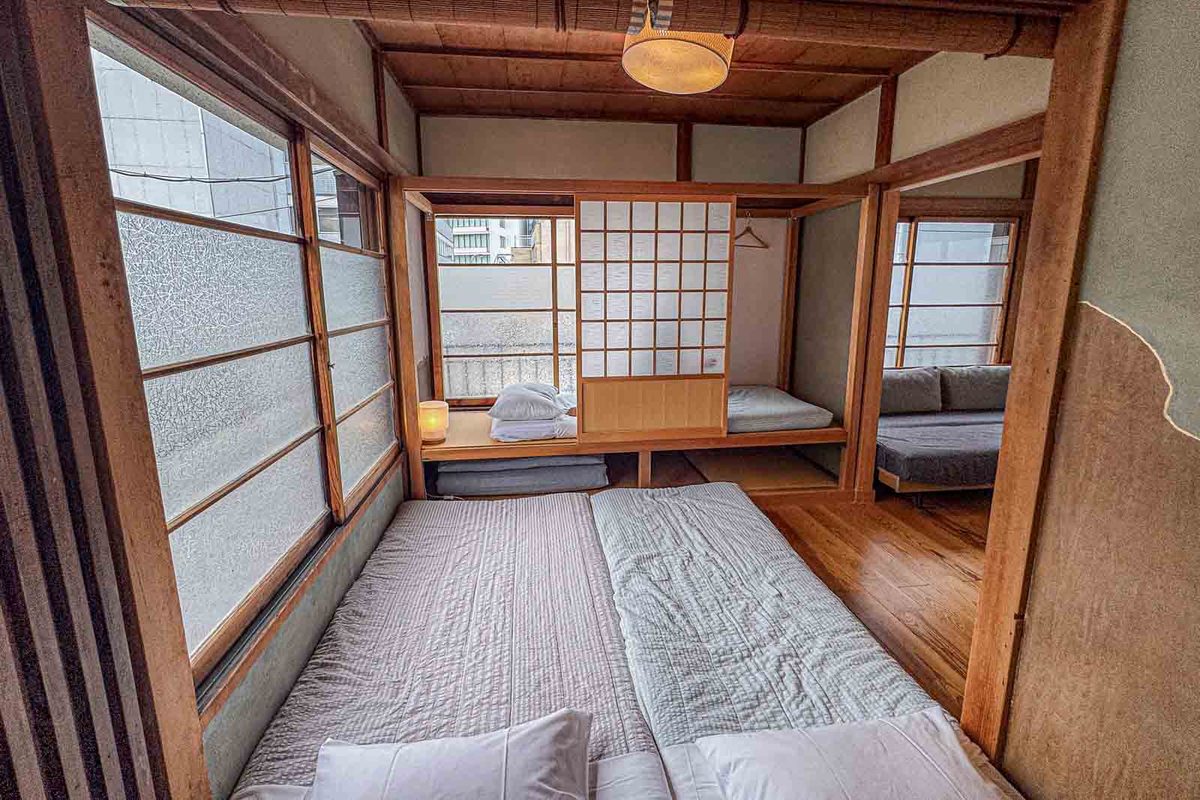Two futon mattresses lie side by side on the floor of a traditional Tokyo townhouse with wood framing and sliding screens. The flexible sleeping area shows how family of 5 travel accommodations can look very different from a standard Western hotel room.