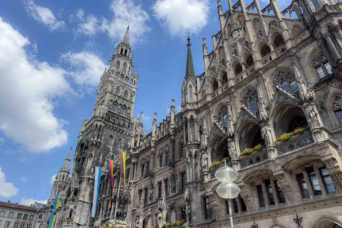 The ornate Gothic Revival facade of Munich New Town Hall in Marienplatz with tall pointed towers and intricate stone carvings beneath a partly cloudy blue sky. One of the main historic landmarks families can explore in Munich Old Town.